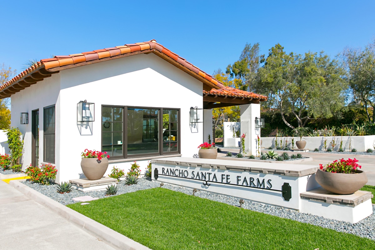 Entrance to Rancho Santa Fe Farms featuring Spanish-style architecture, landscaped gardens, and the community signage set against a clear blue sky.