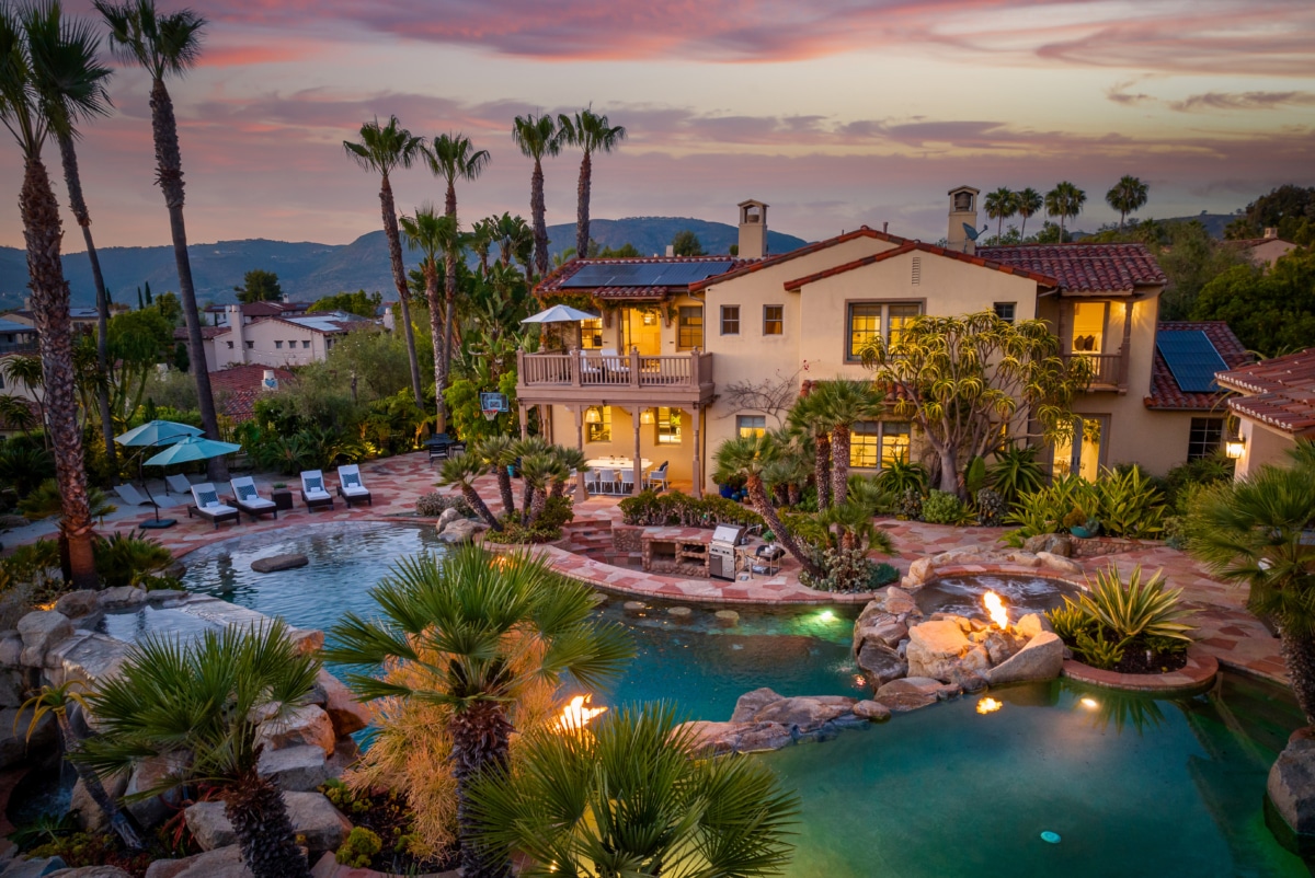 Luxury estate at sunset in The Crosby at Rancho Santa Fe featuring a resort-style backyard with multi-level pool, spa, fire features, and palm-lined landscape