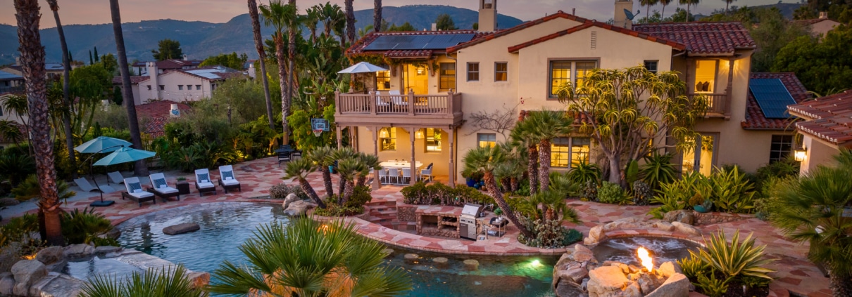 Luxury estate at sunset in The Crosby at Rancho Santa Fe featuring a resort-style backyard with multi-level pool, spa, fire features, and palm-lined landscape