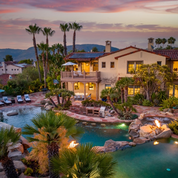 Luxury estate at sunset in The Crosby at Rancho Santa Fe featuring a resort-style backyard with multi-level pool, spa, fire features, and palm-lined landscape
