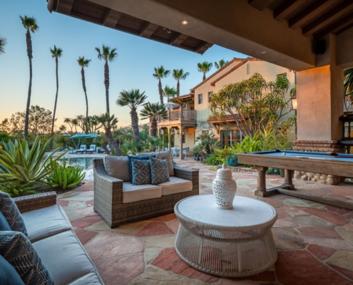 Covered outdoor living space with seating area and pool table overlooking landscaped backyard and pool Covered outdoor living space with seating area and pool table overlooking landscaped backyard and pool