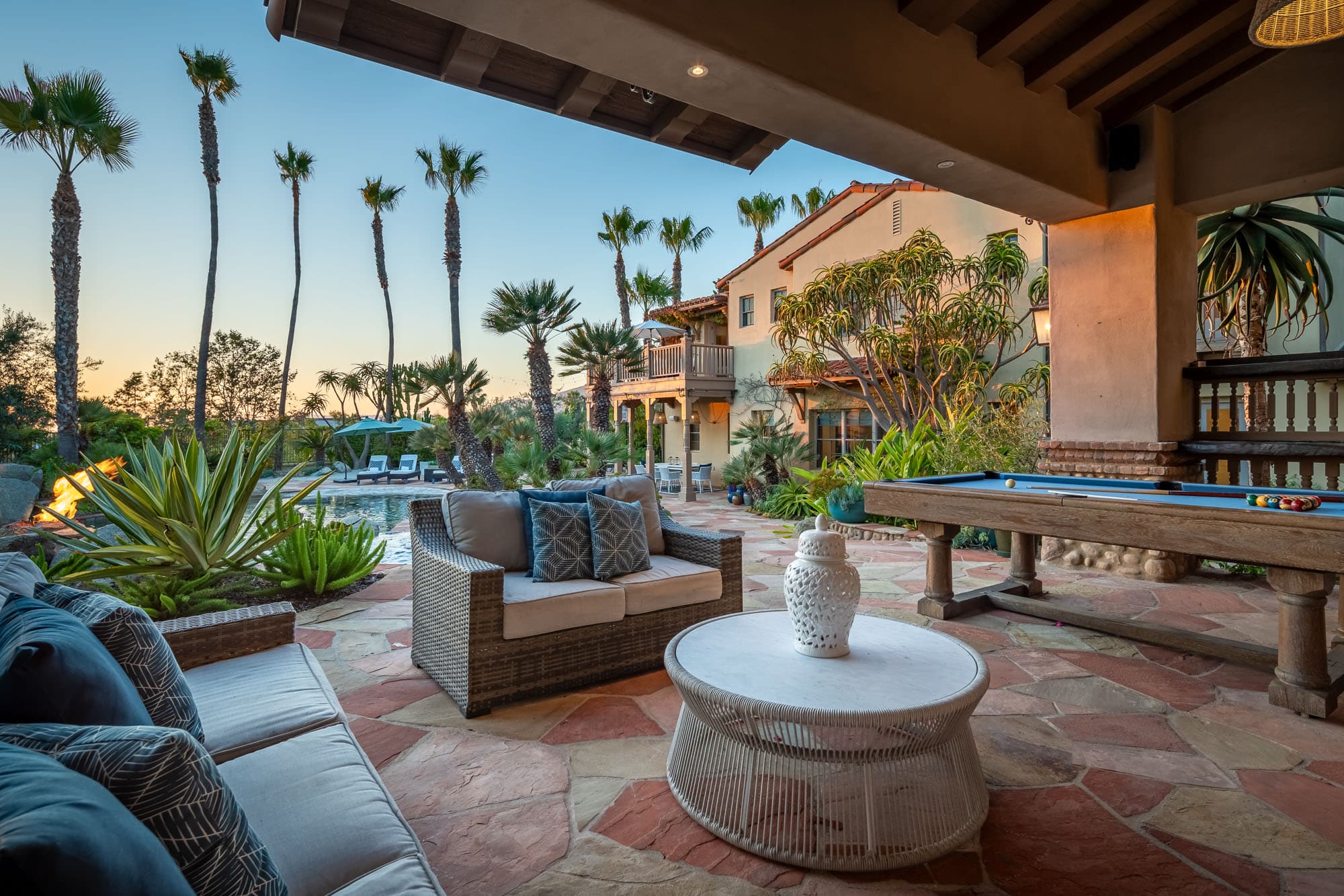 Covered outdoor living space with seating area and pool table overlooking landscaped backyard and pool Covered outdoor living space with seating area and pool table overlooking landscaped backyard and pool