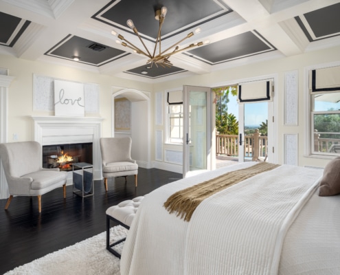 Elegant bedroom with coffered ceiling, statement chandelier, fireplace seating, and French doors opening to a private balcony Elegant bedroom with coffered ceiling, statement chandelier, fireplace seating, and French doors opening to a private balcony