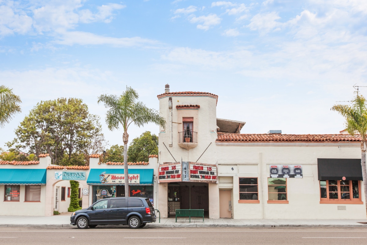 Historic La Paloma Theatre in Encinitas with Spanish-style architecture, tiled roof, palm trees, and storefronts along Coast Highway