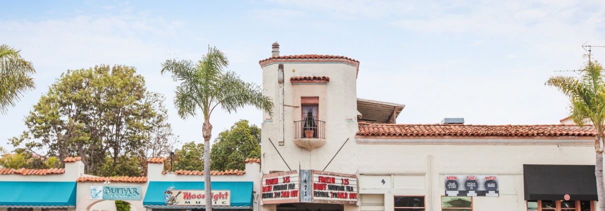 Historic La Paloma Theatre in Encinitas with Spanish-style architecture, tiled roof, palm trees, and storefronts along Coast Highway