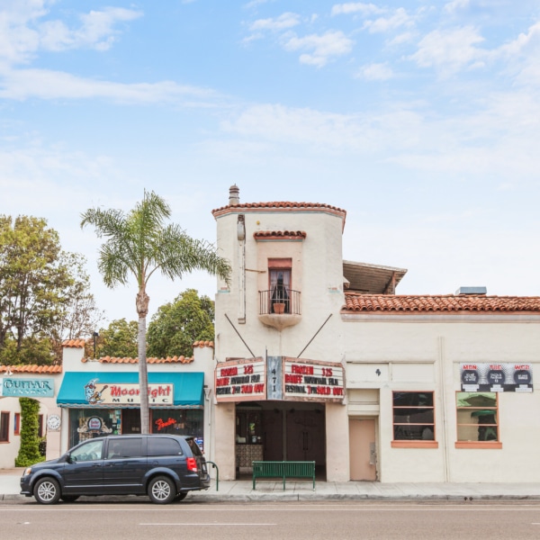Historic La Paloma Theatre in Encinitas with Spanish-style architecture, tiled roof, palm trees, and storefronts along Coast Highway
