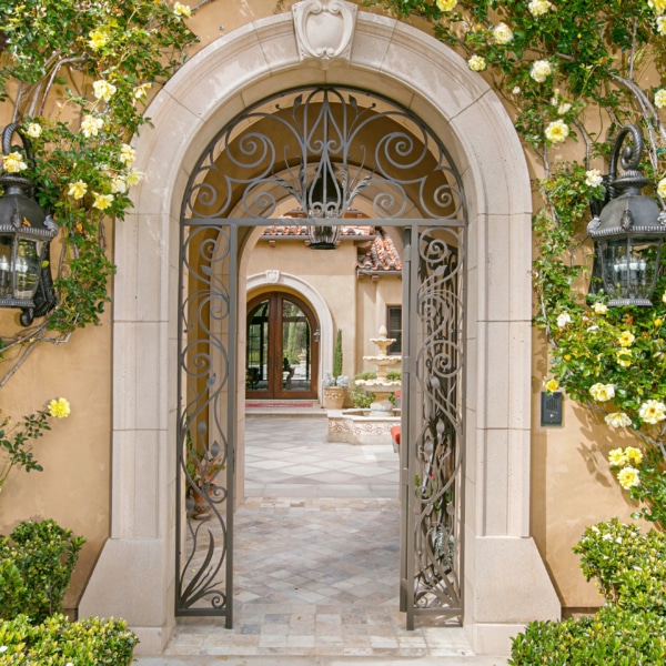 Arched garden entry of a Rancho Santa Fe estate with wrought iron gate, climbing roses, stonework, and landscaped courtyard