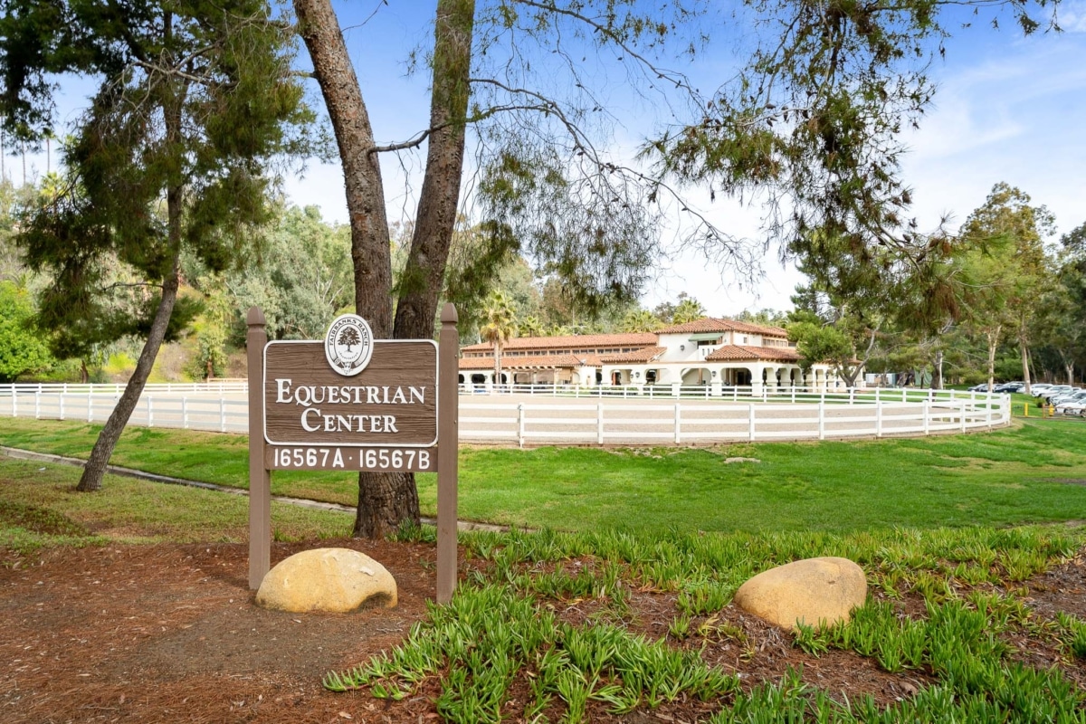 Sign for the Rancho Santa Fe Equestrian Center with paddocks, fencing, and historic buildings in the background