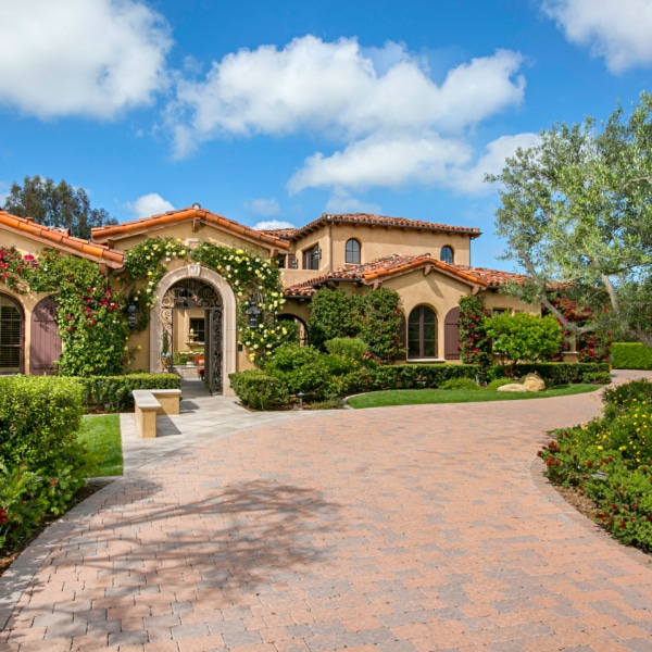 Mediterranean-style estate exterior in Rancho Santa Fe with landscaped gardens, arched entry, and tiled roof under a blue sky