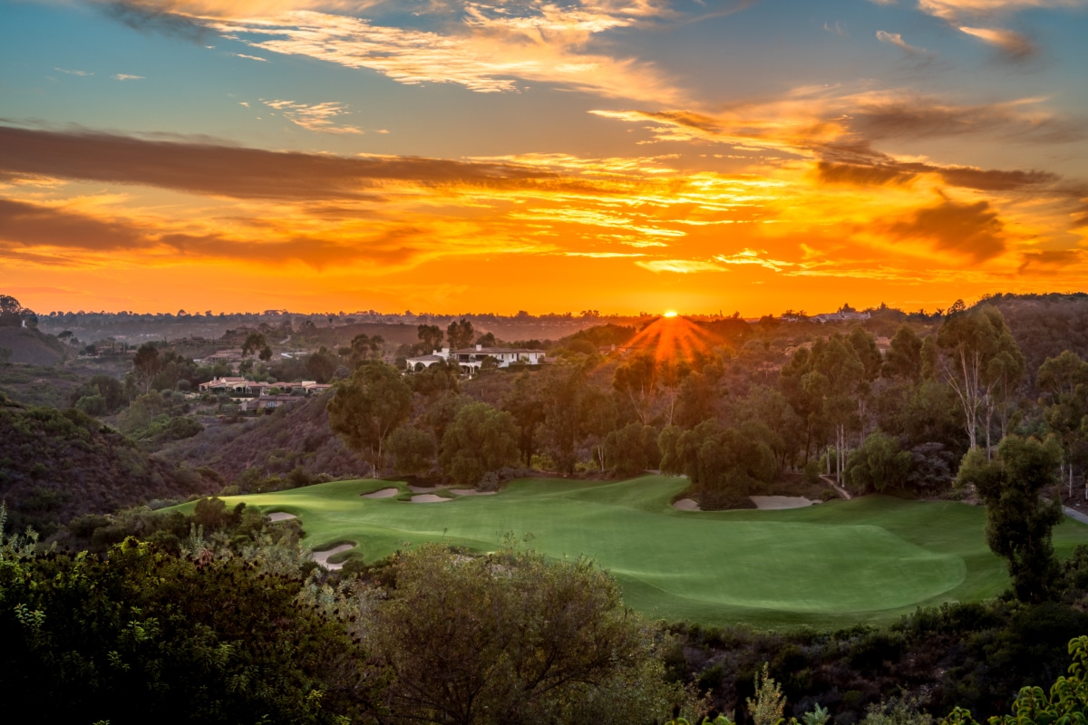 Sunset over a shared green landscape with rolling hills, trees, and open space connecting homes and community land
