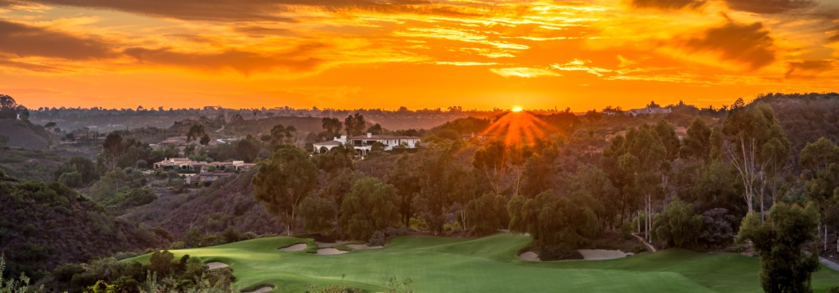 Sunset over a shared green landscape with rolling hills, trees, and open space connecting homes and community land
