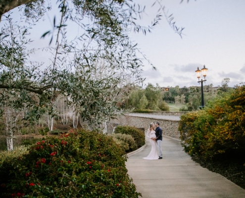 Priscilla and her husband capturing a moment within The Bridges’ landscape Couple walking together along a garden path near a stone bridge at The Bridges Rancho Santa Fe